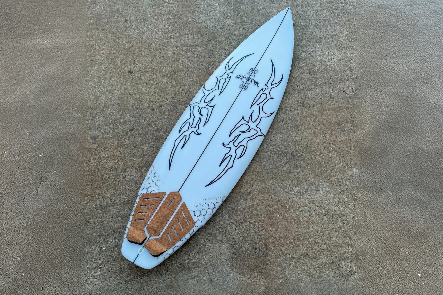 White surfboard with black designs and RSPro cork Tail Grip on a concrete surface